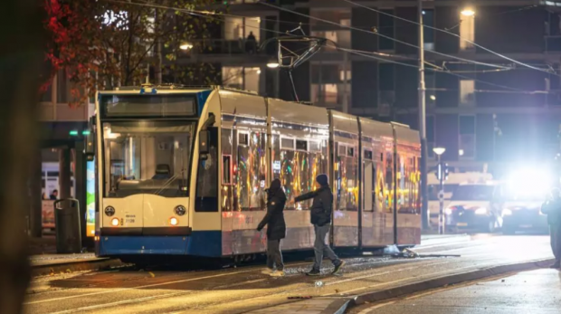 Pedestres se aproximam de um bonde danificado no distrito de Niew-West, em Amsterdã, depois que um grupo incendiou o veículo com fogos de artifício, em 11 de novembro de 2024. AFP - TALHA ANDAC