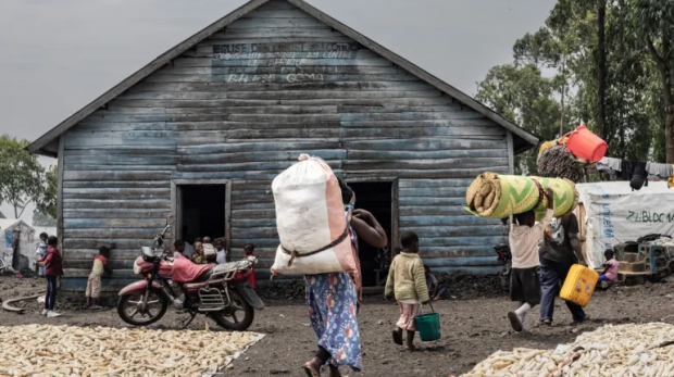 Deslocados internos carregam alguns de seus pertences enquanto passam pela Igreja CBCA Mugunga, localizada no campo de deslocados internos de Mugunga em Goma [Michel Lunanga / AFP]